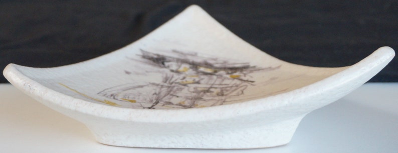 May include: A white ceramic dish with a triangular shape and a subtle, abstract design in shades of gray and yellow.