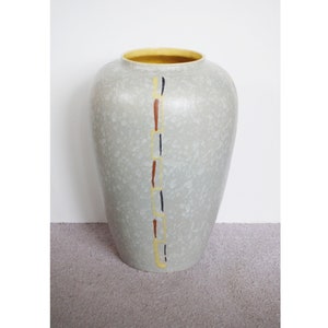 May include: A grey ceramic vase with a speckled glaze and a yellow rim. The vase has a vertical design of yellow, orange, and blue lines.