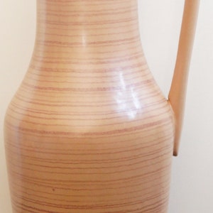 Puede incluir: Un jarr&oacute;n alto de cer&aacute;mica marr&oacute;n con un patr&oacute;n de veta de madera y una sola asa. El jarr&oacute;n tiene un cuerpo redondeado y un cuello estrecho.