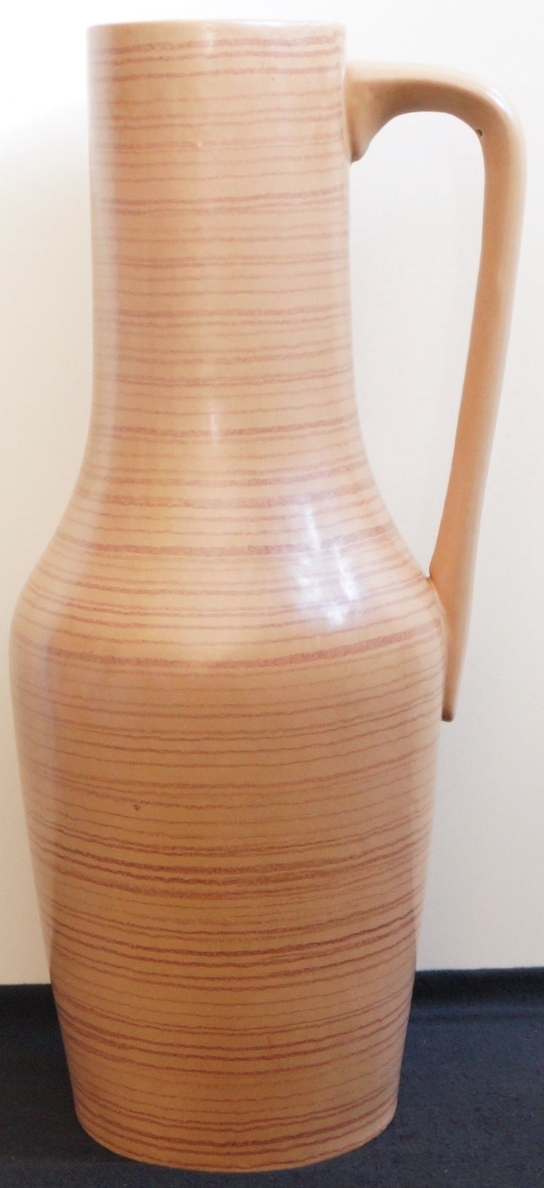 Puede incluir: Un jarr&oacute;n alto de cer&aacute;mica marr&oacute;n con un patr&oacute;n de veta de madera y una sola asa. El jarr&oacute;n tiene un cuerpo redondeado y un cuello estrecho.