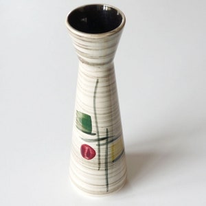May include: A white ceramic vase with a black rim and abstract geometric designs in green, red, and yellow.