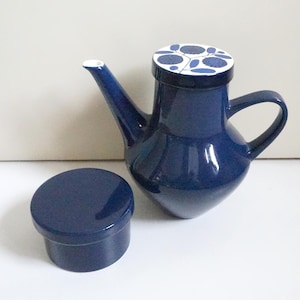 Op de afbeelding: Een marineblauwe keramische theepot met een bijpassend deksel en een kleine, ronde container. De theepot heeft een gebogen handvat en een lange tuit. Het deksel heeft een witte achtergrond met blauwe bloemmotieven. De container is effen marineblauw.