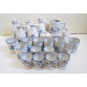 Op de afbeelding: Een set van 18 keramische stukken in een wit en blauw kleurenschema. De set bevat een verscheidenheid aan serveerstukken, waaronder kannen, kruiken en kleine kopjes. De stukken zijn versierd met een bloemenpatroon en een zwanenontwerp.