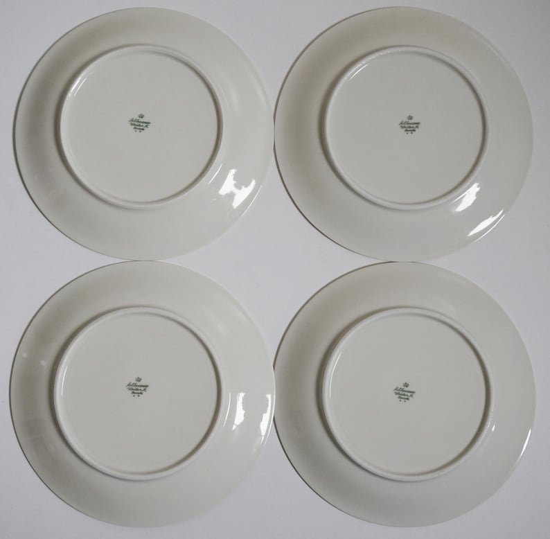 May include: Four white ceramic dinner plates with a green and gold logo that reads "Jobst Germany" on the bottom.