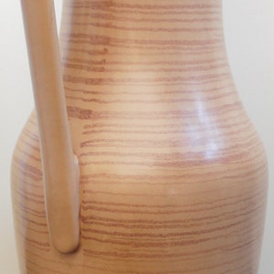 Puede incluir: Una jarra de cer&aacute;mica marr&oacute;n con un patr&oacute;n de veta de madera y un asa. La jarra es alta y estrecha con una base redondeada.