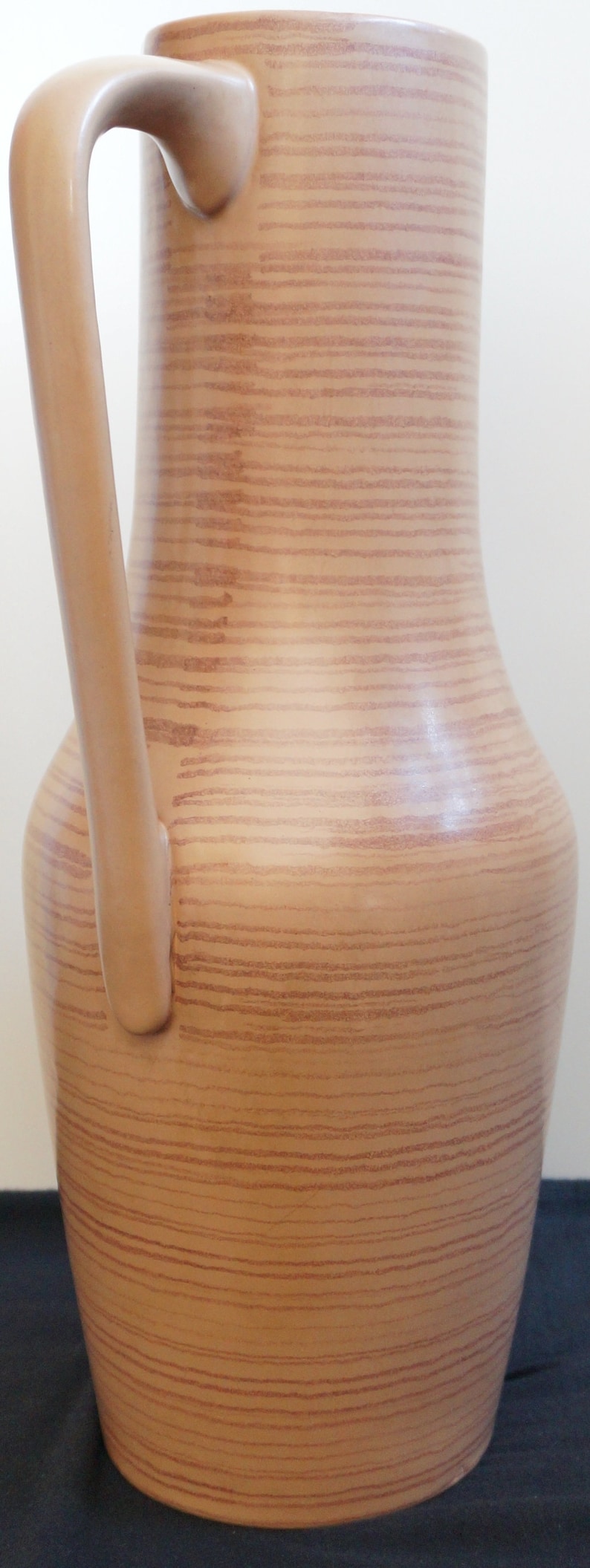 Puede incluir: Una jarra de cer&aacute;mica marr&oacute;n con un patr&oacute;n de veta de madera y un asa. La jarra es alta y estrecha con una base redondeada.