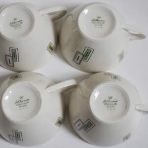 May include: Set of four white ceramic teacups with a geometric design in shades of green, blue, yellow, and pink. The bottom of each cup has the text "Johannisthaler Walter K. Bavaria" in black.