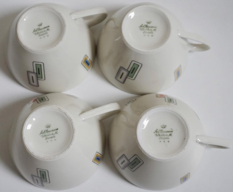 May include: Set of four white ceramic teacups with a geometric design in shades of green, blue, yellow, and pink. The bottom of each cup has the text "Johannisthaler Walter K. Bavaria" in black.