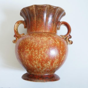 May include: A brown ceramic vase with two handles and a speckled glaze. The vase has a wide mouth and a rounded body.