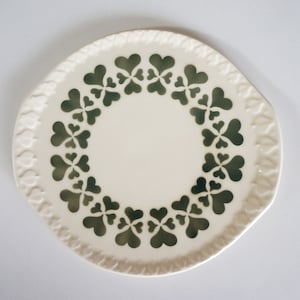 Peut inclure: Une assiette en céramique blanche avec un motif de trèfles verts autour du bord.