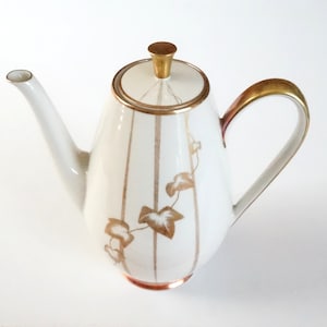 Op de afbeelding: Witte porseleinen theepot met een gouden rand en een gouden bladontwerp. De theepot heeft een gouden knop op de deksel en een gouden handvat.