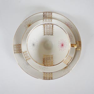 Peut inclure: Une tasse à thé et une soucoupe blanches avec un motif géométrique doré et rose. L'ensemble présente un délicat motif floral avec une bordure dorée.