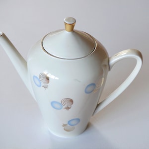 Op de afbeelding: Witte porseleinen koffiekan met een gouden rand en een abstract ontwerp in blauw en bruin.