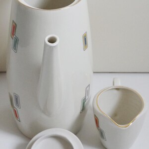 May include: A white ceramic coffee pot with a lid and a matching creamer. The pot has a geometric pattern of colorful squares.