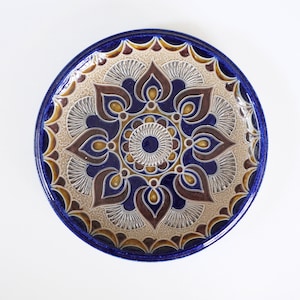 May include: A blue and brown ceramic plate with a decorative floral pattern. The plate has a raised design and a glossy finish.