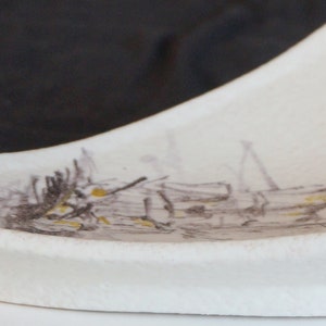 May include: A white ceramic dish with a triangular shape and a textured surface. The dish has a subtle design of brown and black lines and shapes.