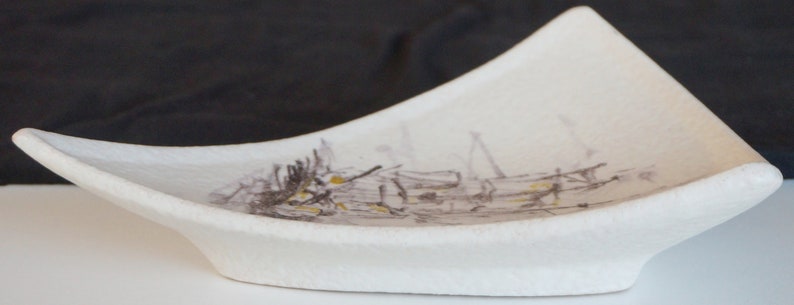 May include: A white ceramic dish with a triangular shape and a textured surface. The dish has a subtle design of brown and black lines and shapes.
