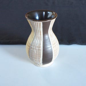 以下が含まれることがあります： 茶色の内側とテクスチャ加工された外側を備えた、小さな装飾用の花瓶。 花瓶は、クリーム、茶色、白の垂直方向のリブのディテールが特徴です。濃い茶色のストライプが前面を走っています。