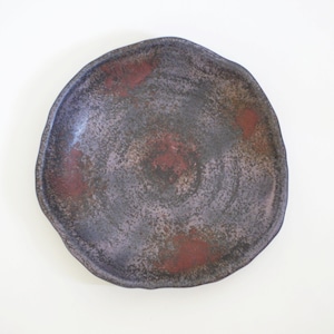 Può includere: Un piatto in ceramica fatto a mano con una forma organica e irregolare. Il piatto presenta una superficie macchiata e strutturata con una tavolozza di colori grigio scuro, viola e rosso. Il diametro del piatto è di circa 25 cm.