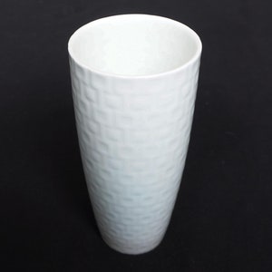 May include: White ceramic vase with a textured, embossed pattern. The vase has a cylindrical shape and a smooth, rounded rim.