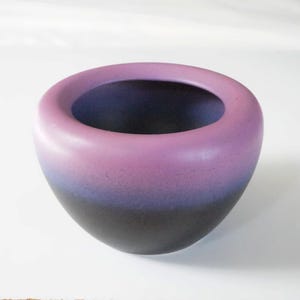 Op de afbeelding: Een keramische kom met een gladde, afgeronde vorm. De kom heeft een kleurengradiënt, van diepzwart aan de basis naar tinten blauw en paars, eindigend met een zachtroze rand. De binnenkant is donkerblauw.