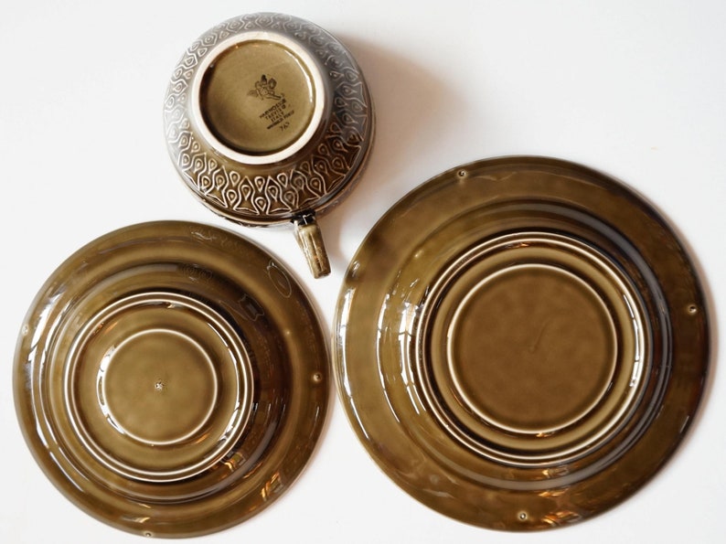 May include: A set of three brown ceramic plates with a concentric circle design. The largest plate is 25 cm in diameter. The smallest plate is 15 cm in diameter. The cup is 10 cm in diameter. The cup has a brown glaze with a floral design and the text "Made in England" on the bottom.