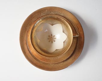 Puede incluir: Un juego de taza y platillo de té dorado y blanco con un patrón geométrico. La taza tiene un diseño en forma de flor con un copo de nieve en el centro.