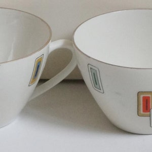 May include: Set of four white ceramic teacups with a geometric design in shades of orange, green, and blue.