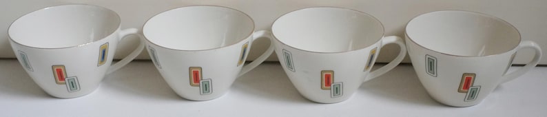 May include: Set of four white ceramic teacups with a geometric design in shades of orange, green, and blue.