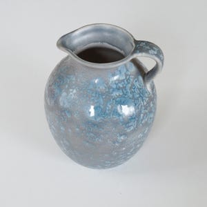 May include: A ceramic jug with a rounded body and a handle. The jug is mainly grey with blue and white mottled patterns. The rim and handle are a solid grey-blue colour. The jug has a spout for pouring.