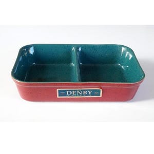 May include: A rectangular ceramic divided serving dish with a speckled teal interior and a solid red exterior. A rectangular blue and white label on the front features the text THE DENBY POTTERY COMPANY LTD with the years 1809 and 2009.