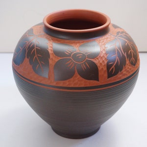 Op de afbeelding: Een bruine keramische vaas met een decoratief ontwerp van bladeren en bloemen. De vaas heeft een brede opening en een rond lichaam.