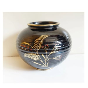May include: A black ceramic vase with gold and red floral designs. The vase has a round body and a slightly flared rim.