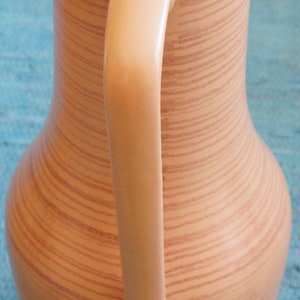 Puede incluir: Una jarra de cer&aacute;mica marr&oacute;n claro con un patr&oacute;n de veta de madera y un asa. La jarra tiene una boca ancha y un cuerpo redondeado.