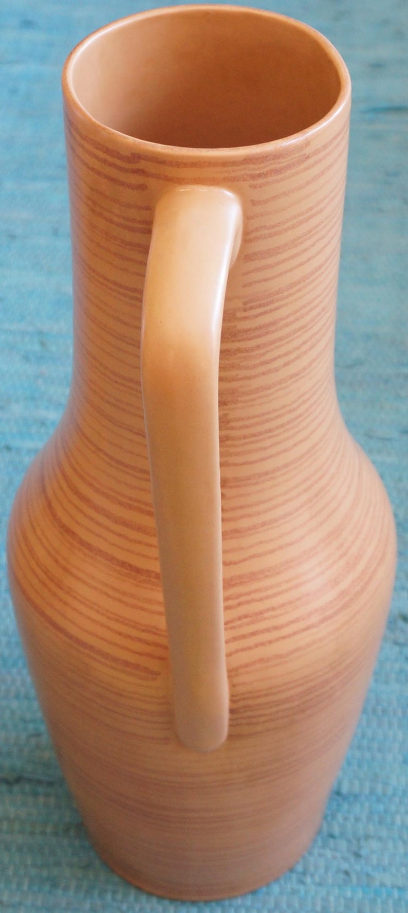 Puede incluir: Una jarra de cer&aacute;mica marr&oacute;n claro con un patr&oacute;n de veta de madera y un asa. La jarra tiene una boca ancha y un cuerpo redondeado.