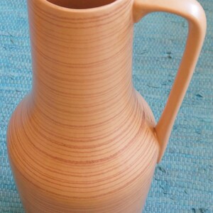 Puede incluir: Un jarr&oacute;n alto de cer&aacute;mica marr&oacute;n con un patr&oacute;n de veta de madera y un asa. El jarr&oacute;n tiene una base ancha y un cuello estrecho.