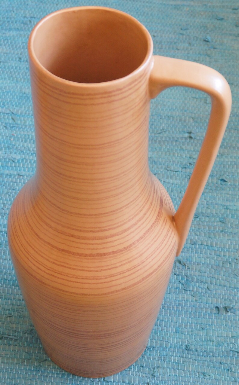 Puede incluir: Un jarr&oacute;n alto de cer&aacute;mica marr&oacute;n con un patr&oacute;n de veta de madera y un asa. El jarr&oacute;n tiene una base ancha y un cuello estrecho.