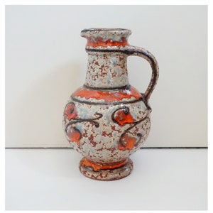 May include: A small, white ceramic jug with a crackled glaze and orange floral designs. The jug has a rounded body and a small handle.