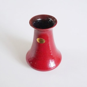 Op de afbeelding: Een rode keramische vaas met een gouden label met de tekst "Handcrafted".