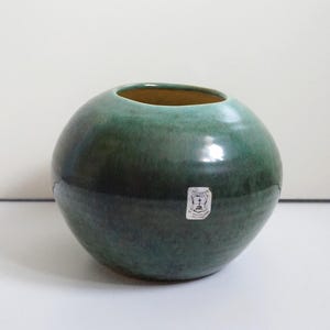 Op de afbeelding: Een bolvormige keramische vaas met een gladde, glanzende afwerking in tinten diep bosgroen en blauwgroen. De vaas heeft een kleine, ronde opening aan de bovenkant en een witte rechthoekige sticker met de tekst 'RUSMAN BY MAASTRICHT HOLLAND'.