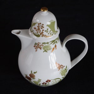 May include: White ceramic teapot with a rounded body, a curved handle, and a lid topped with a gold knob. The teapot is decorated with green, gold, and brown floral patterns. The spout is on the left side.