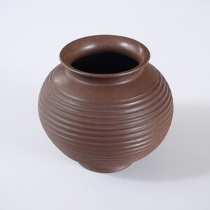 Op de afbeelding: Een bruine keramische vaas met een rond lichaam en een geribbelde textuur.