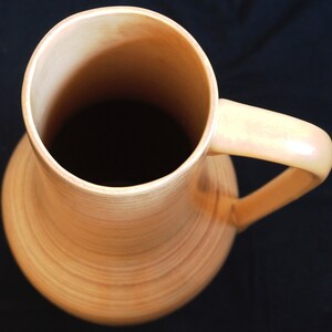 Puede incluir: Un jarr&oacute;n de cer&aacute;mica de color crema, alto y de boca ancha, con una sola asa. El jarr&oacute;n tiene una textura acanalada y un acabado brillante.