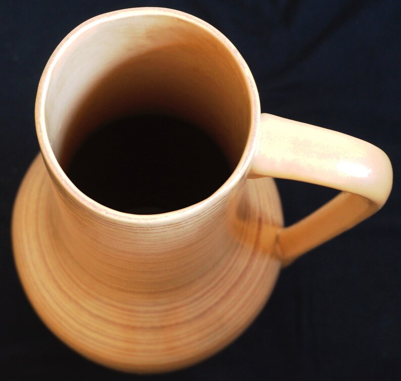 Puede incluir: Un jarr&oacute;n de cer&aacute;mica de color crema, alto y de boca ancha, con una sola asa. El jarr&oacute;n tiene una textura acanalada y un acabado brillante.