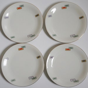 May include: Four white ceramic plates with gold trim and colorful geometric designs. Each plate has a different arrangement of the designs.