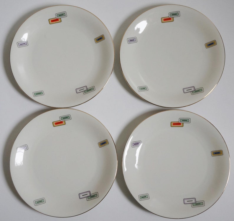 May include: Four white ceramic plates with gold trim and colorful geometric designs. Each plate has a different arrangement of the designs.
