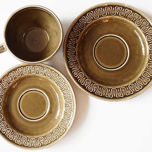 May include: A set of three brown ceramic teacups and saucers with a white, decorative pattern. The cups and saucers have a glossy finish.