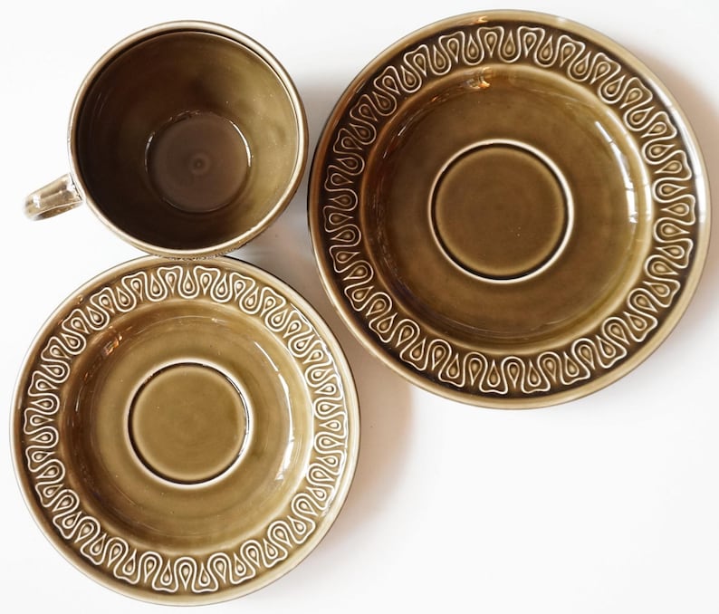 May include: A set of three brown ceramic teacups and saucers with a white, decorative pattern. The cups and saucers have a glossy finish.