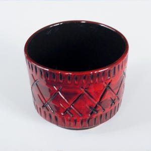 Op de afbeelding: Een rode keramische plantenpot met een zwarte binnenkant en een ruitvormig ontwerp.