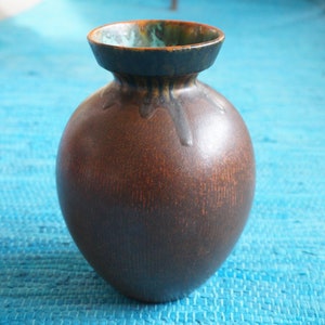 Op de afbeelding: Een bruine keramische vaas met een groene en bruine geglazuurde rand. De vaas heeft een rond lichaam en een smalle hals.